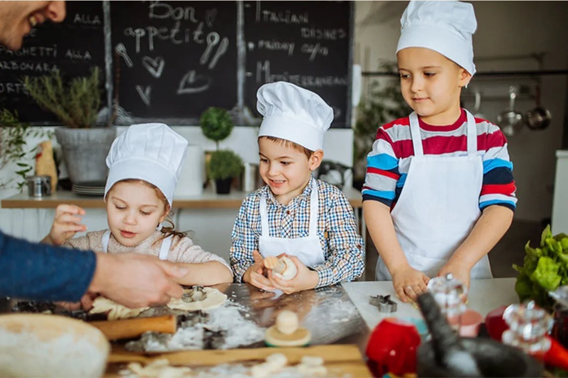 Trois enfants en toque décorent des biscuits pendant un atelier
